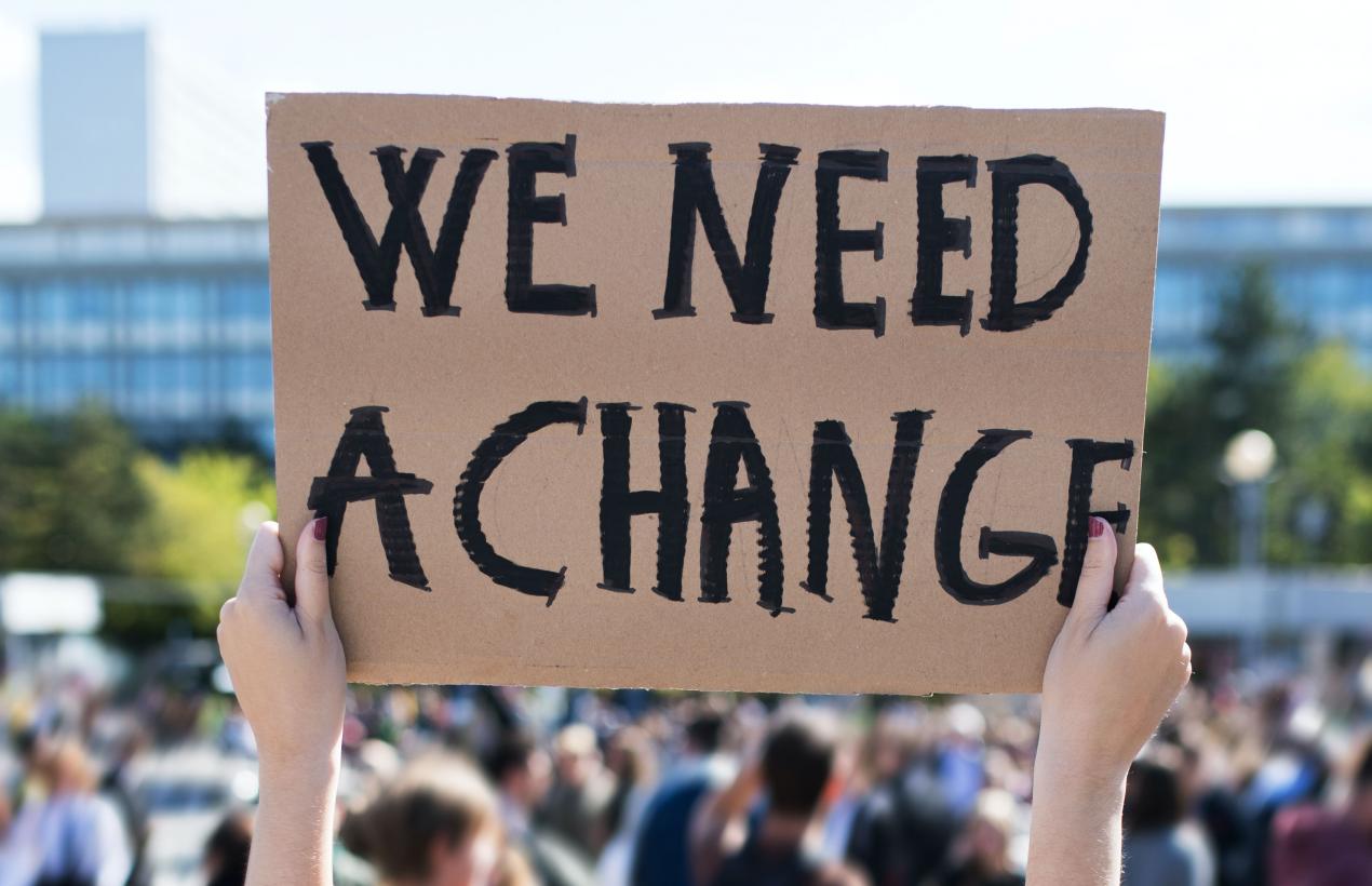 Image of protestors carrying a sign that says "We Need a Change"