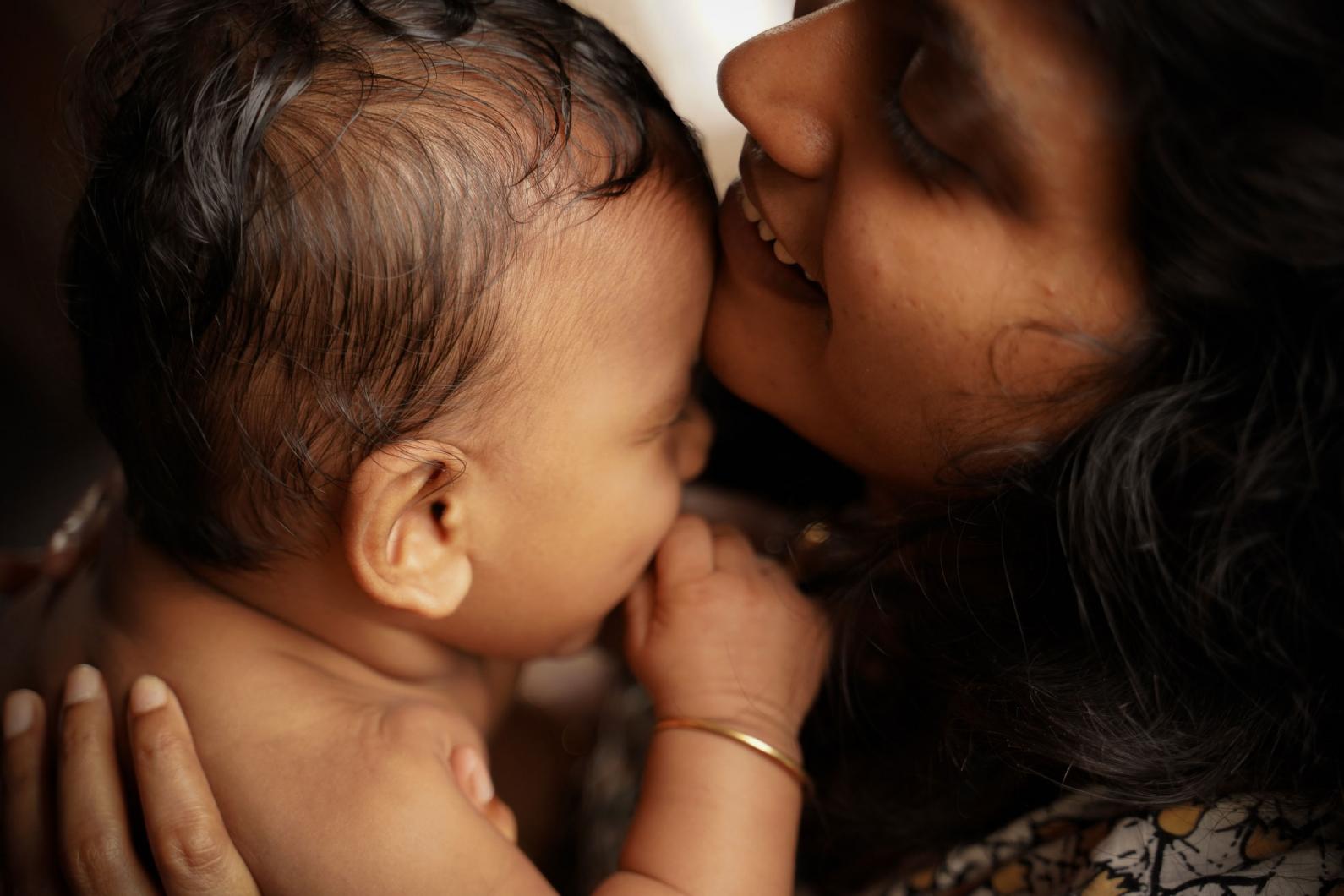 Woman holding her baby close and placing her chin on its forehead.