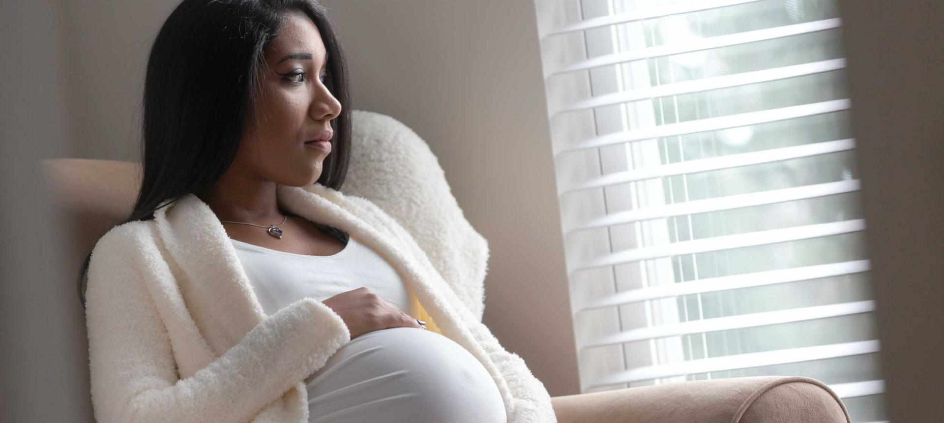 A pregnant woman of color looking out the window