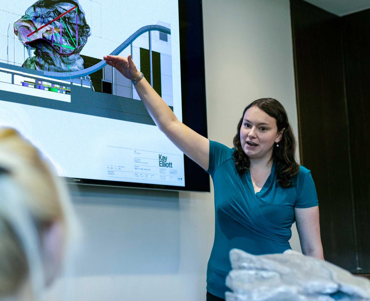 White woman pointing at a video screen during a presentation